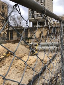 view through chain link fence to construction area with mounds of dirt and pipes waiting to be laid down.