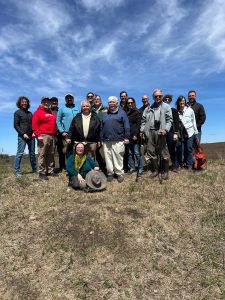 The group at the field trip to Westport Drumlin Prairie stands in the sun with a blue sky behind them.