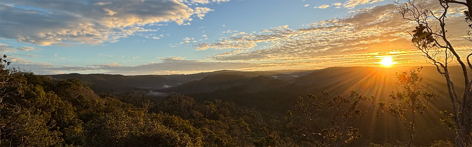 The sun rises over a mountainous Hawaii terrain.